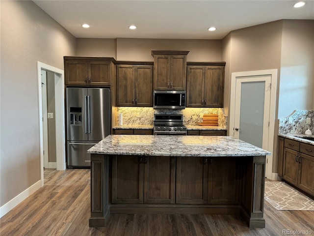 kitchen featuring dark brown cabinetry, light stone countertops, dark wood-type flooring, stainless steel appliances, and a kitchen island