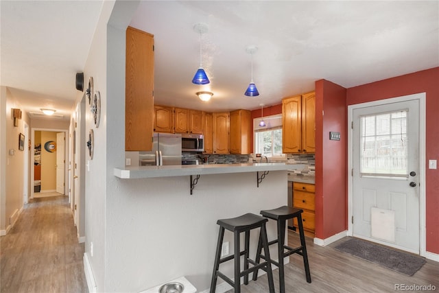 11805 W 74th Ave, Arvada, CO 80005 - kitchen featuring appliances with stainless steel finishes, light wood-style flooring, a kitchen bar, light countertops, and a peninsula
