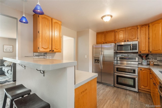 11805 W 74th Ave, Arvada, CO 80005 - kitchen with appliances with stainless steel finishes, a kitchen breakfast bar, light wood-style floors, a peninsula, and light countertops
