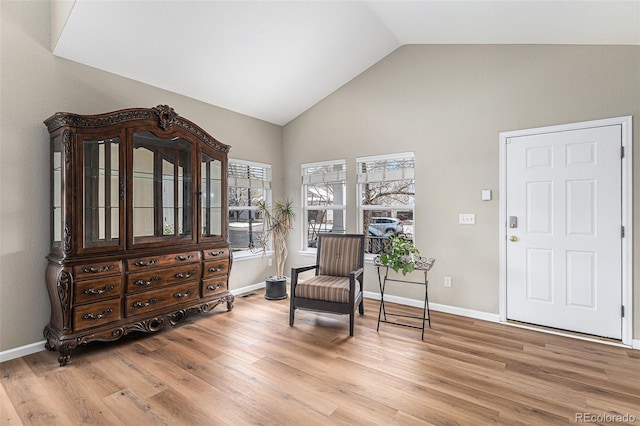 living area with high vaulted ceiling, baseboards, and light wood-style floors