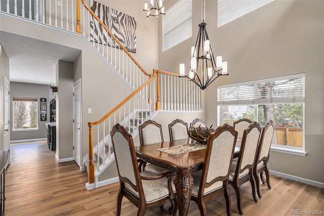 dining area with a high ceiling, baseboards, a chandelier, light wood-style flooring, and stairs