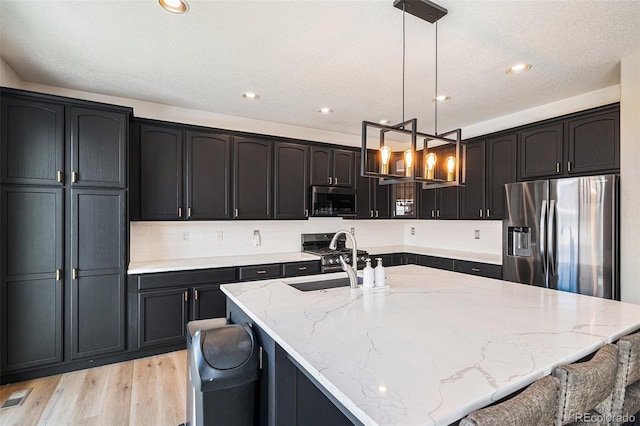 kitchen with light stone counters, a large island, stainless steel appliances, a sink, and light wood-style flooring