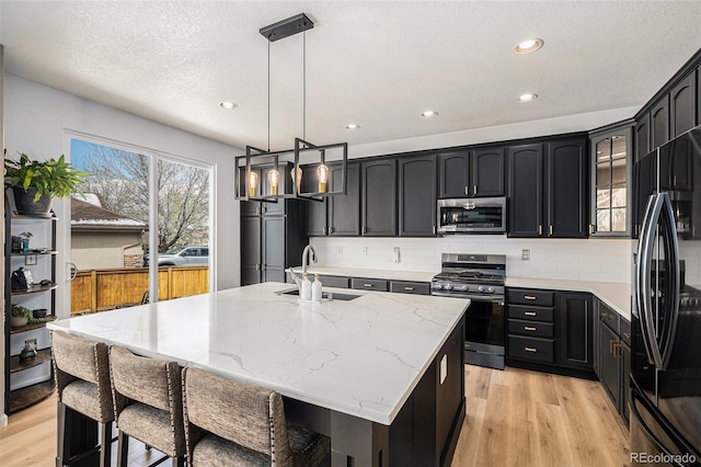 kitchen featuring light stone counters, stainless steel appliances, dark cabinetry, a sink, and light wood-style floors