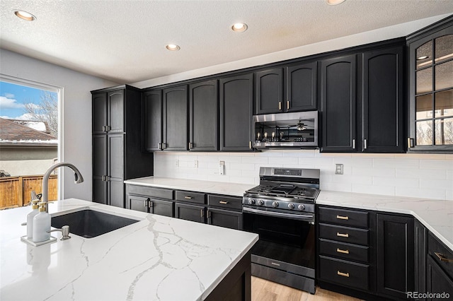 kitchen featuring light stone counters, dark cabinetry, stainless steel appliances, and a sink