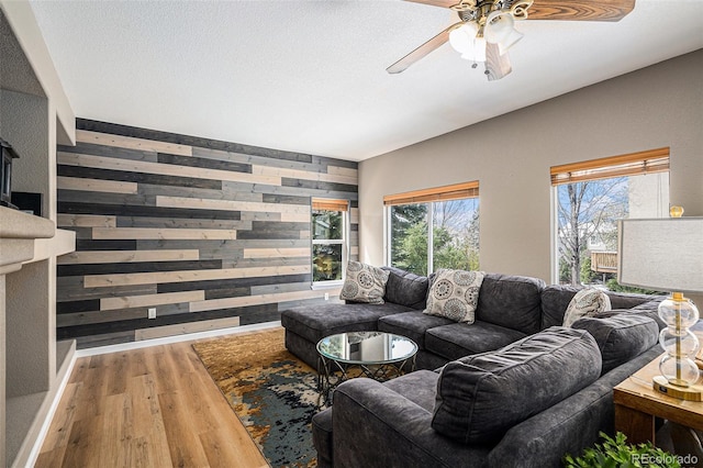 living room with an accent wall, a ceiling fan, wood finished floors, and wooden walls