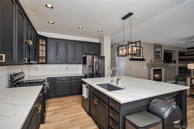9407 W Gibraltar Pl, Littleton, CO 80127 - kitchen with appliances with stainless steel finishes, light wood-style floors, an island with sink, tasteful backsplash, and light stone counters