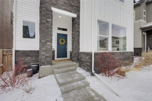 snow covered property entrance with stone siding