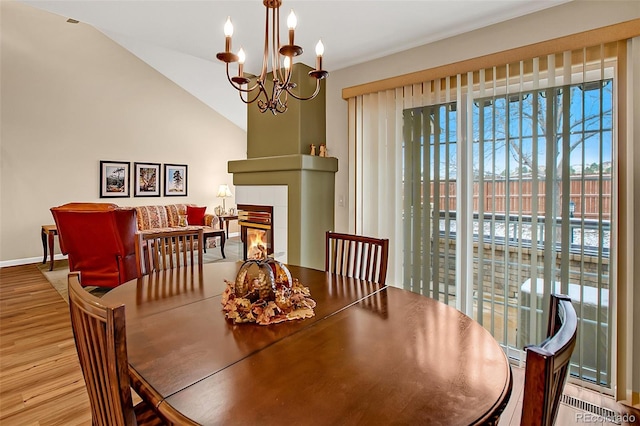 dining area featuring a fireplace, a chandelier, vaulted ceiling, and light hardwood / wood-style flooring