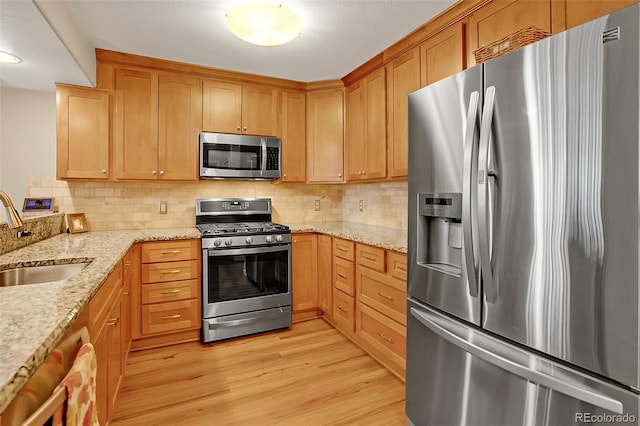 kitchen with sink, tasteful backsplash, light stone countertops, light wood-type flooring, and appliances with stainless steel finishes