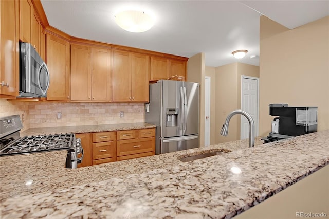 kitchen with stainless steel appliances, sink, kitchen peninsula, light stone counters, and tasteful backsplash