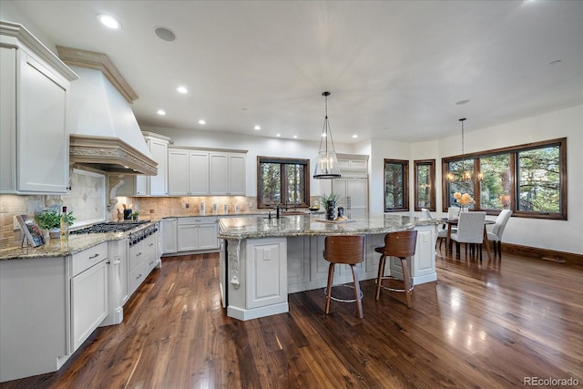 kitchen with white cabinetry, backsplash, pendant lighting, a center island with sink, and custom exhaust hood