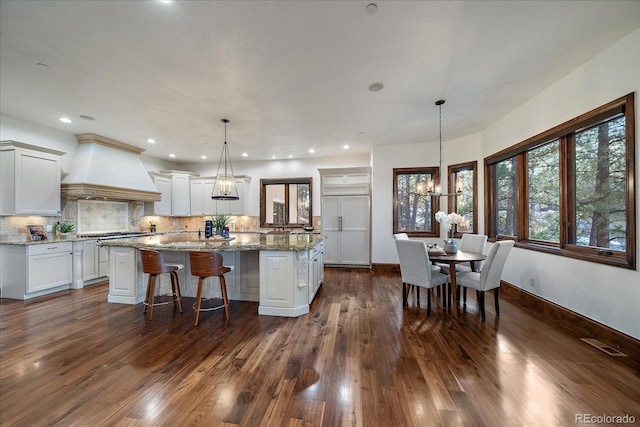 kitchen with light stone counters, a chandelier, decorative light fixtures, a kitchen island, and custom exhaust hood