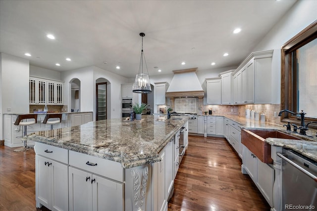 kitchen with custom exhaust hood, backsplash, decorative light fixtures, a large island, and stainless steel appliances