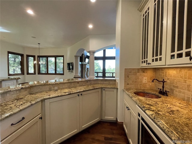 kitchen featuring ornate columns, light stone countertops, sink, dark hardwood / wood-style flooring, and backsplash