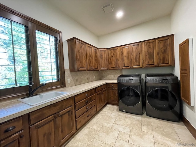 clothes washing area with washer and dryer, light tile patterned floors, cabinets, and sink