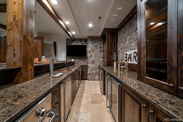 bar with dark brown cabinetry, sink, beverage cooler, and dark stone counters