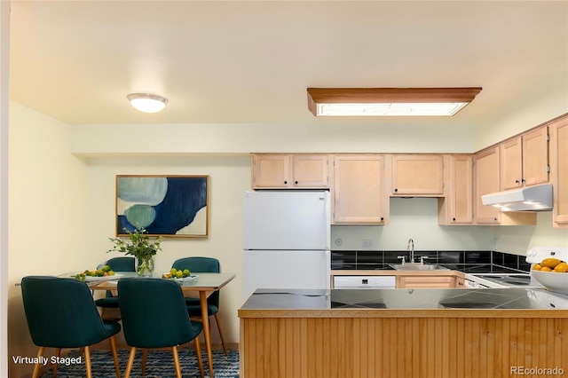 kitchen featuring a peninsula, light brown cabinets, white appliances, under cabinet range hood, and a sink