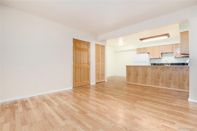unfurnished living room with baseboards, a sink, and light wood finished floors