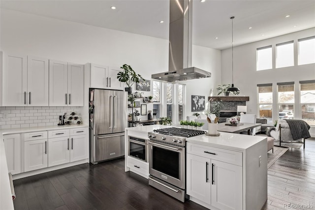 kitchen with high end appliances, white cabinetry, island range hood, decorative light fixtures, and a high ceiling