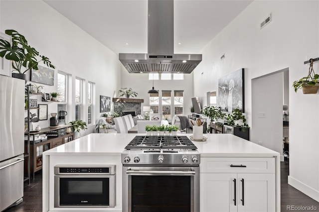 kitchen featuring dark wood-type flooring, appliances with stainless steel finishes, a towering ceiling, island exhaust hood, and white cabinets