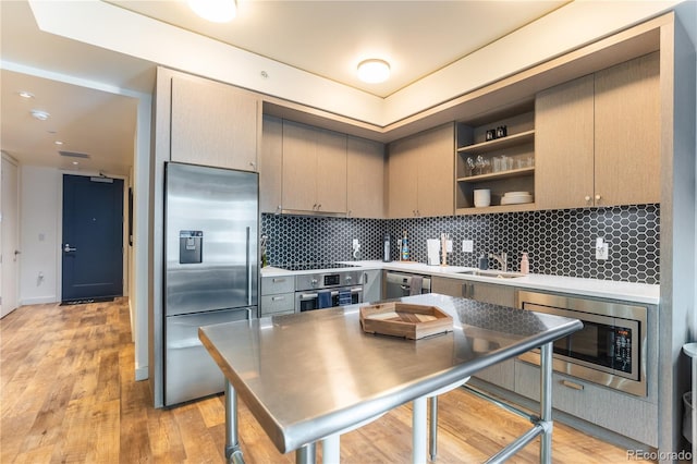 kitchen featuring built in appliances, sink, backsplash, and light hardwood / wood-style flooring