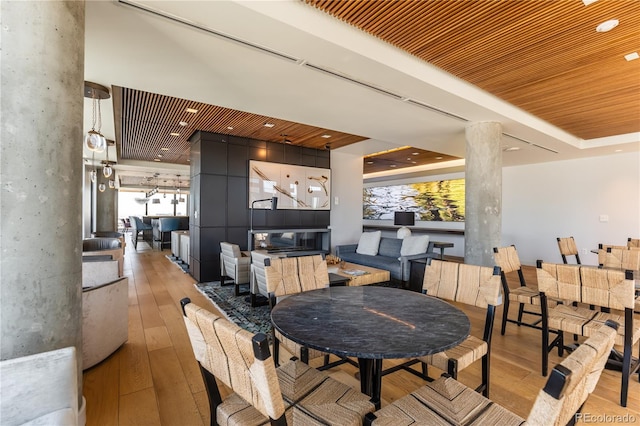 dining space featuring light hardwood / wood-style flooring, wooden ceiling, a raised ceiling, and ornate columns