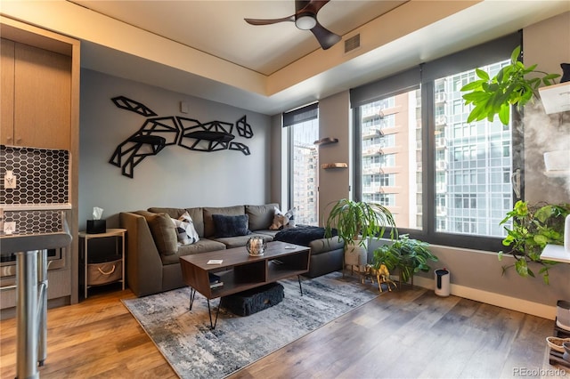 living room with a raised ceiling, hardwood / wood-style floors, and ceiling fan