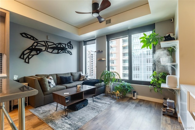 living room with wood-type flooring, ceiling fan, and a tray ceiling