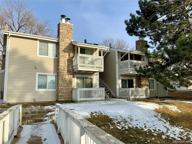 snow covered back of property with a balcony and a chimney