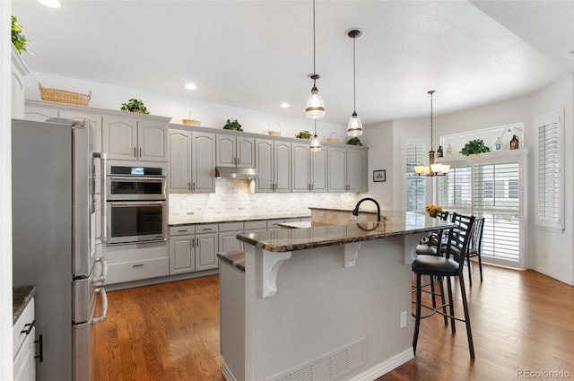 kitchen with gray cabinets, an island with sink, appliances with stainless steel finishes, and a kitchen bar