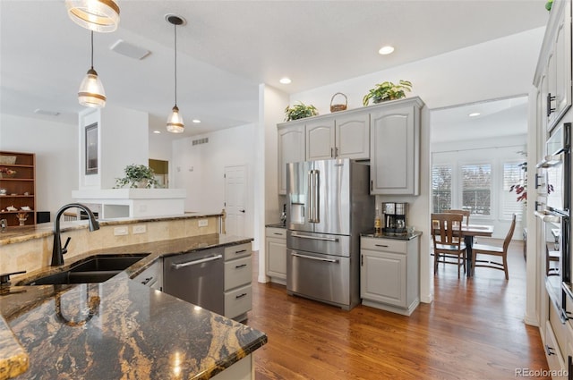 kitchen with sink, hanging light fixtures, appliances with stainless steel finishes, gray cabinets, and dark stone counters