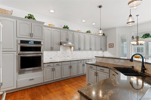 kitchen featuring sink, dark stone counters, hanging light fixtures, and stainless steel double oven