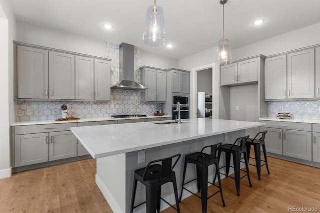 kitchen featuring wall chimney range hood, gas stovetop, gray cabinets, and a sink