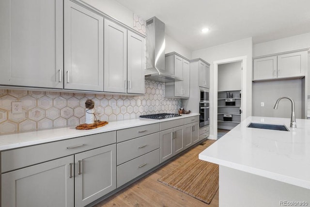 kitchen with stainless steel gas stovetop, gray cabinets, a sink, and wall chimney range hood