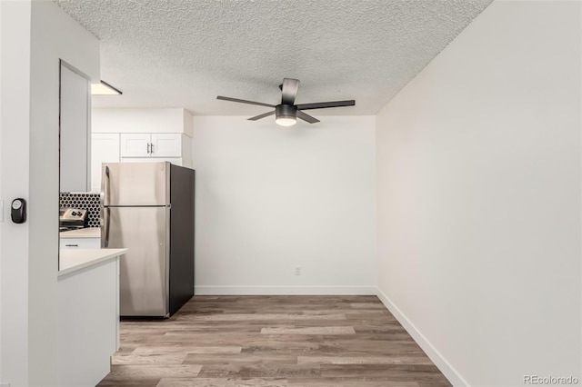 kitchen with light wood-type flooring, white cabinets, stainless steel fridge, ceiling fan, and a textured ceiling