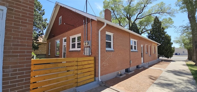 view of home's exterior with fence, a chimney, and brick siding