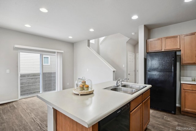 kitchen featuring dark wood-style flooring, an island with sink, light countertops, a sink, and black appliances