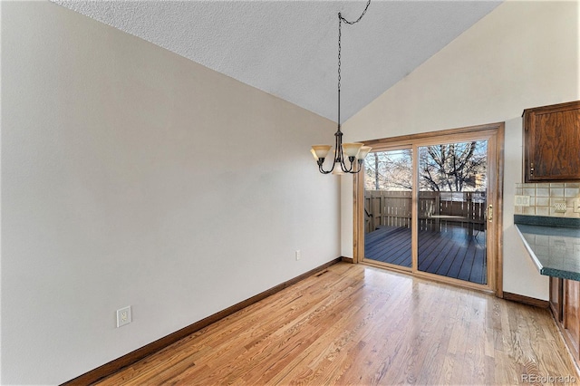 unfurnished dining area with a textured ceiling, light hardwood / wood-style flooring, lofted ceiling, and an inviting chandelier