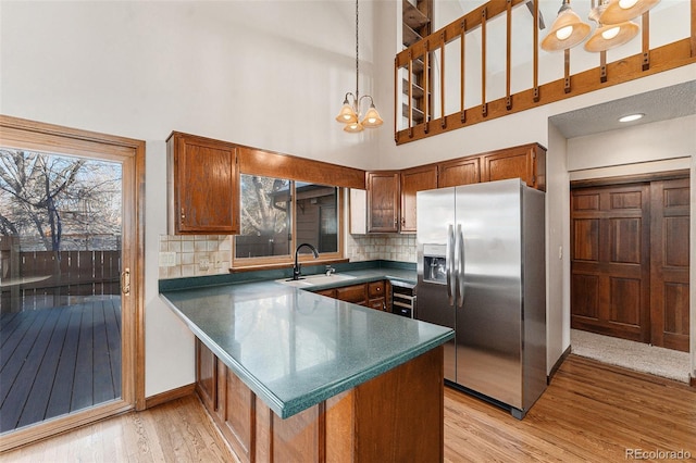 kitchen featuring a towering ceiling, tasteful backsplash, sink, hanging light fixtures, and stainless steel fridge