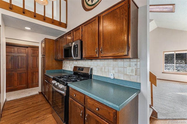 kitchen featuring light hardwood / wood-style floors, stainless steel appliances, decorative backsplash, lofted ceiling, and a textured ceiling