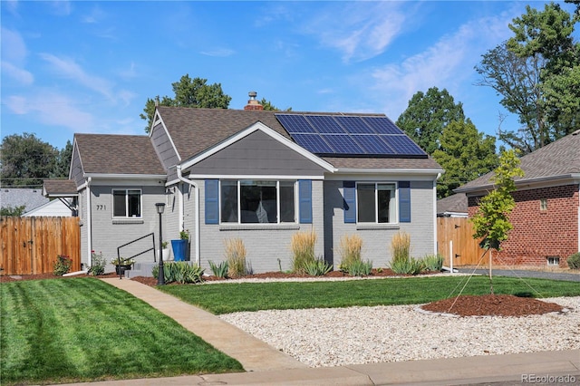 view of front of house featuring fence, a front yard, roof mounted solar panels, brick siding, and a chimney