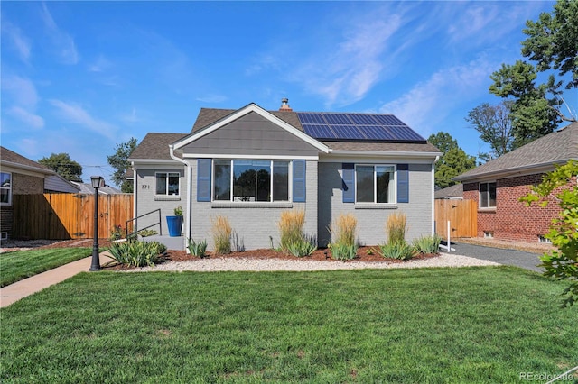 view of front of home featuring fence, brick siding, a front lawn, and solar panels