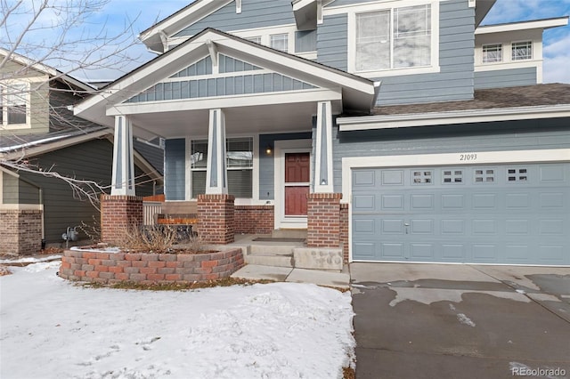 snow covered property entrance featuring a porch and a garage