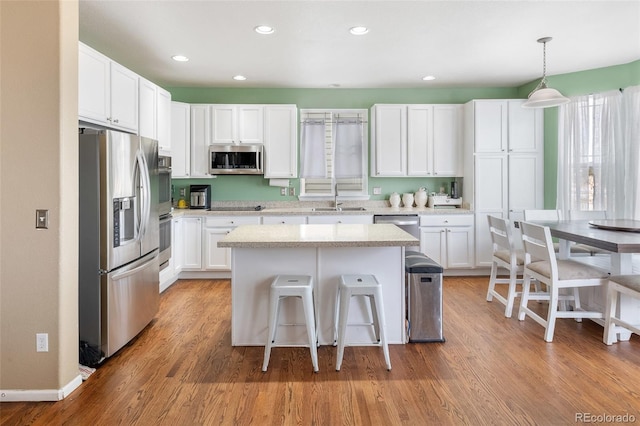 kitchen with a kitchen bar, a sink, a kitchen island, white cabinetry, and stainless steel appliances