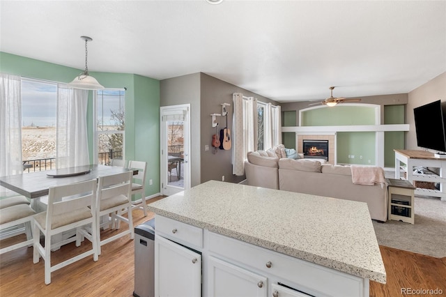 kitchen with a tiled fireplace, hanging light fixtures, light wood-style floors, and white cabinetry