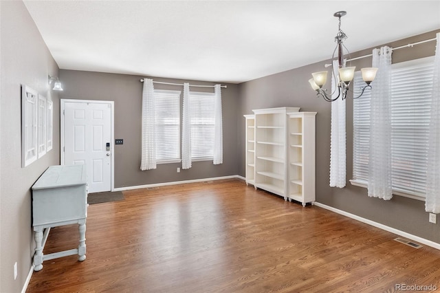 unfurnished dining area with visible vents, baseboards, wood finished floors, and a chandelier