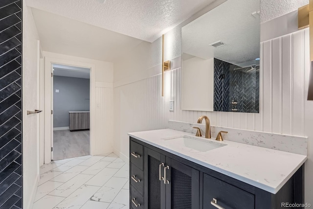 7400 S Genoa Cir, Centennial, CO 80016 - bathroom featuring marble finish floors, a textured ceiling, vanity, tiled shower, and wainscoting