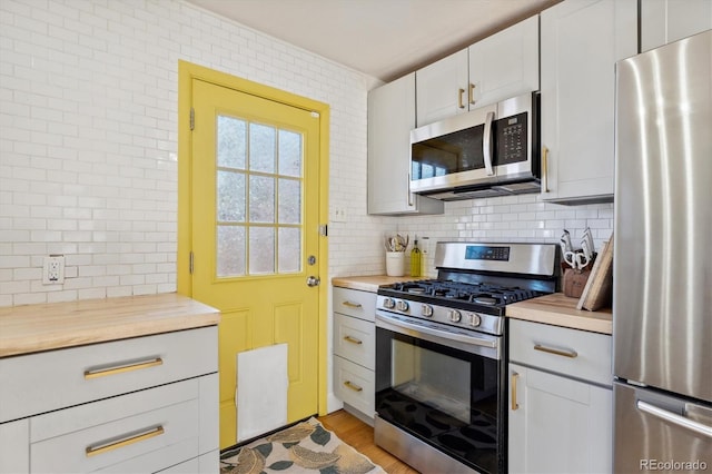 kitchen with butcher block countertops, light hardwood / wood-style flooring, appliances with stainless steel finishes, white cabinetry, and backsplash