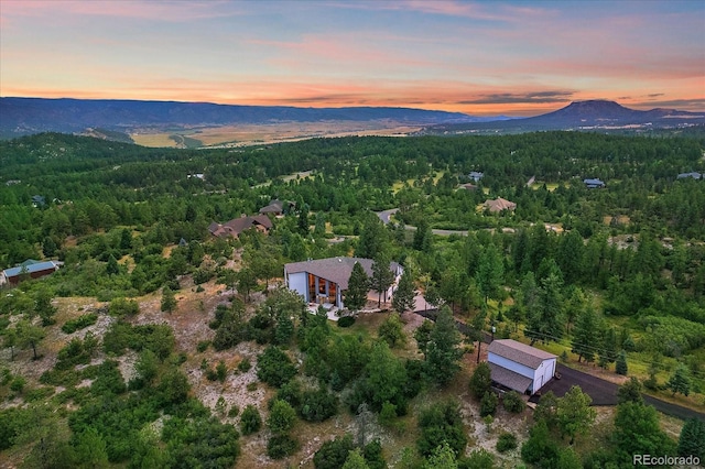 aerial view at dusk featuring a mountain view and a view of trees