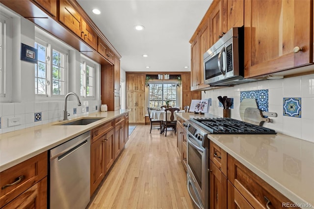 kitchen with stainless steel appliances, sink, light hardwood / wood-style flooring, and backsplash